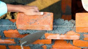 Hands laying bricks with cement in a construction setting, showcasing precise masonry work.